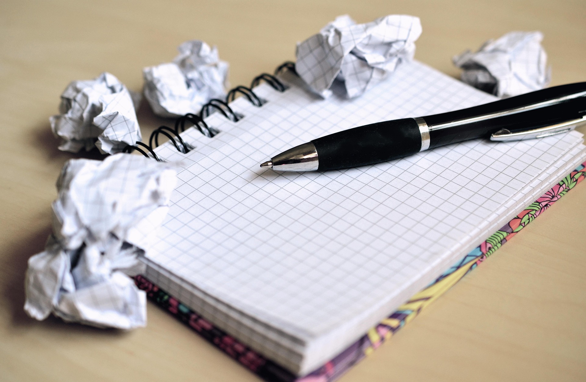 A grid notebook surrounded by crumpled paper balls with a pen resting on the page