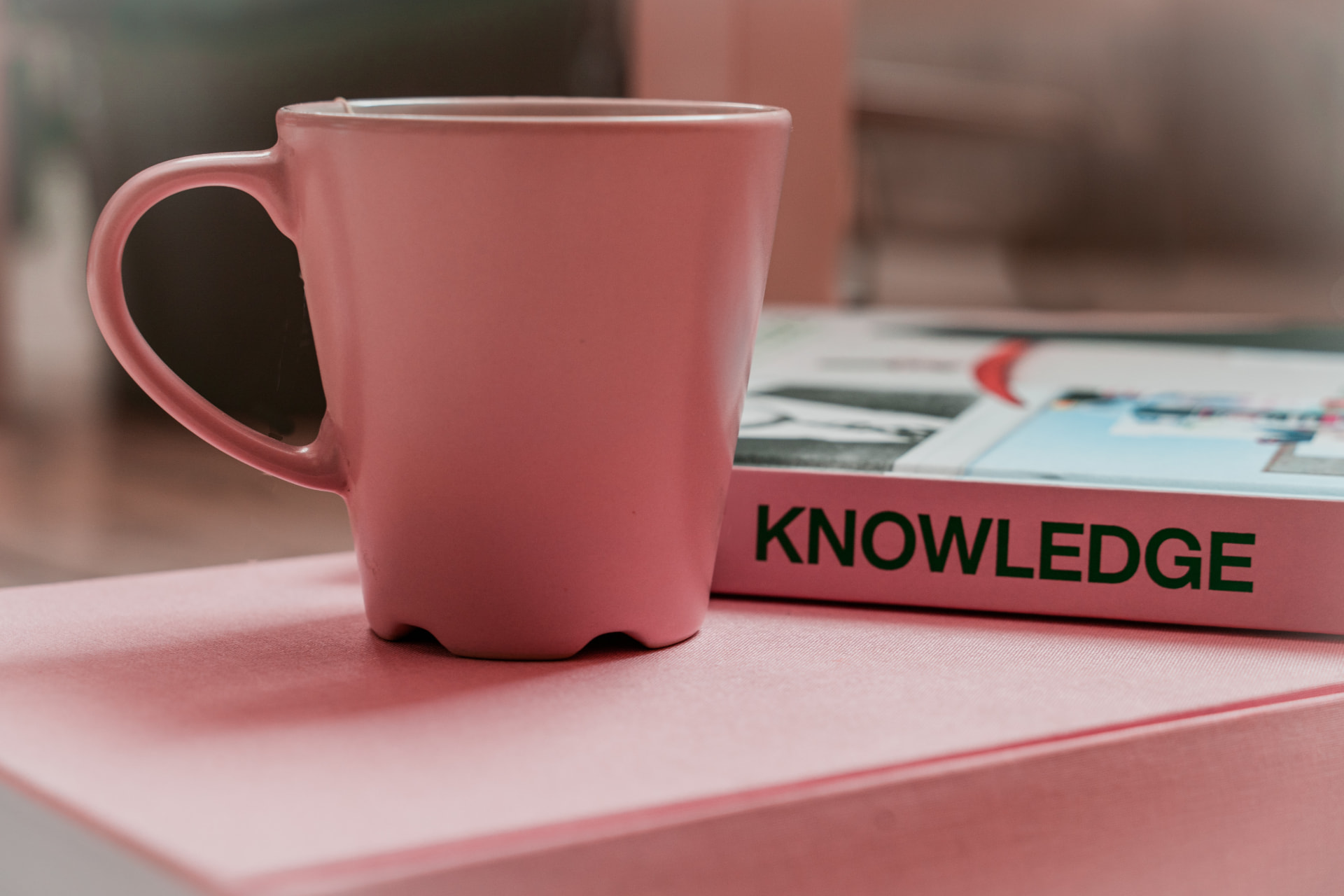 A pink mug resting on a book beside a magazine titled Knowledge